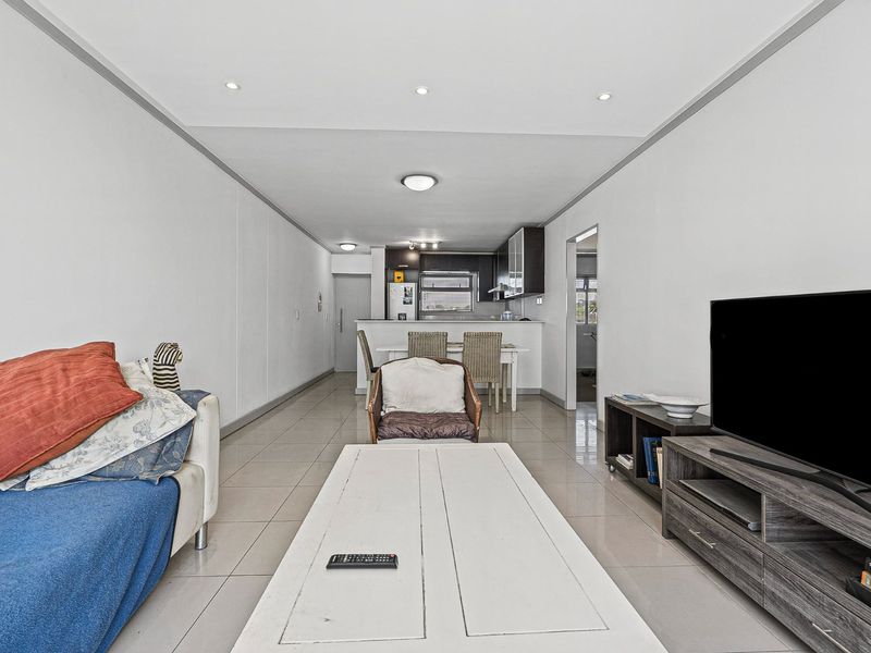 Open-plan living and kitchen area featuring tiled flooring, recessed lighting, and a functional kitchen layout with a breakfast bar.