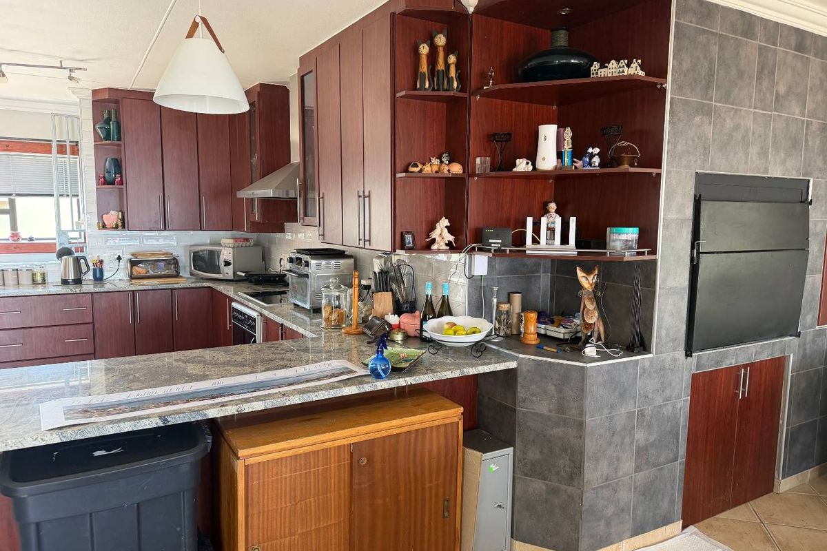 A functional kitchen featuring dark wood cabinetry, granite countertops, and a built-in indoor braai area with tiled surround.