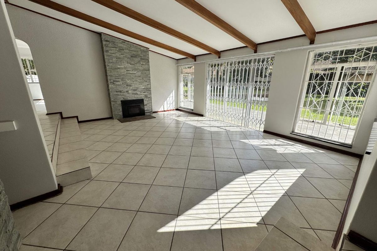Spacious living room featuring tiled flooring, exposed timber ceiling beams, a stone-clad fireplace, and large glass sliding doors with security gates.