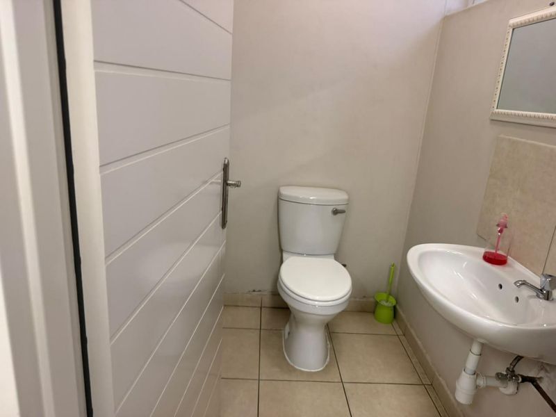 A compact office restroom featuring a standard toilet, pedestal washbasin, and tiled flooring.
