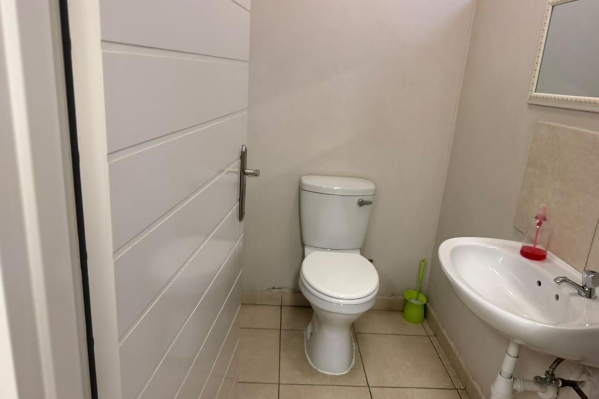 A compact office restroom featuring a standard toilet, pedestal washbasin, and tiled flooring.