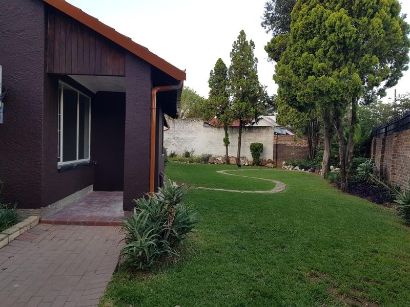 A well-maintained rear garden featuring a paved walkway, tiled patio area, and established lawn enclosed by a secure boundary wall.