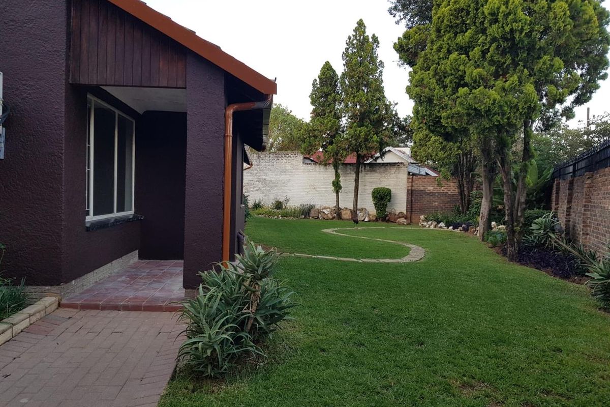 A well-maintained rear garden featuring a paved walkway, tiled patio area, and established lawn enclosed by a secure boundary wall.