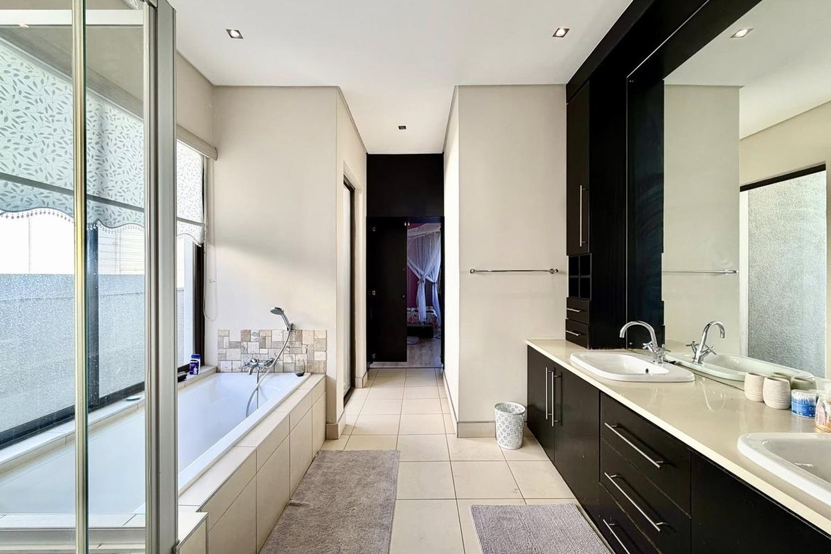 Modern bathroom featuring a built-in bathtub, dual vanity with dark cabinetry, large wall mirror, and tiled flooring.