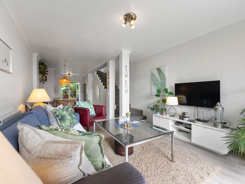Open plan living area featuring painted brick walls, laminate flooring, and a central staircase leading to the upper level.