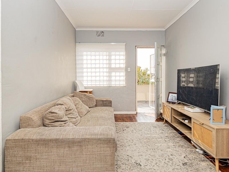 A living room featuring timber flooring, neutral wall finishes, and direct access to an outdoor balcony area through a security door.