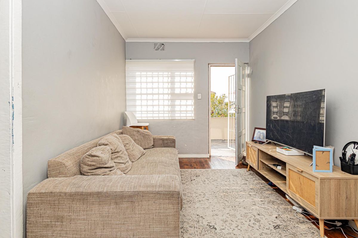A living room featuring timber flooring, neutral wall finishes, and direct access to an outdoor balcony area through a security door.