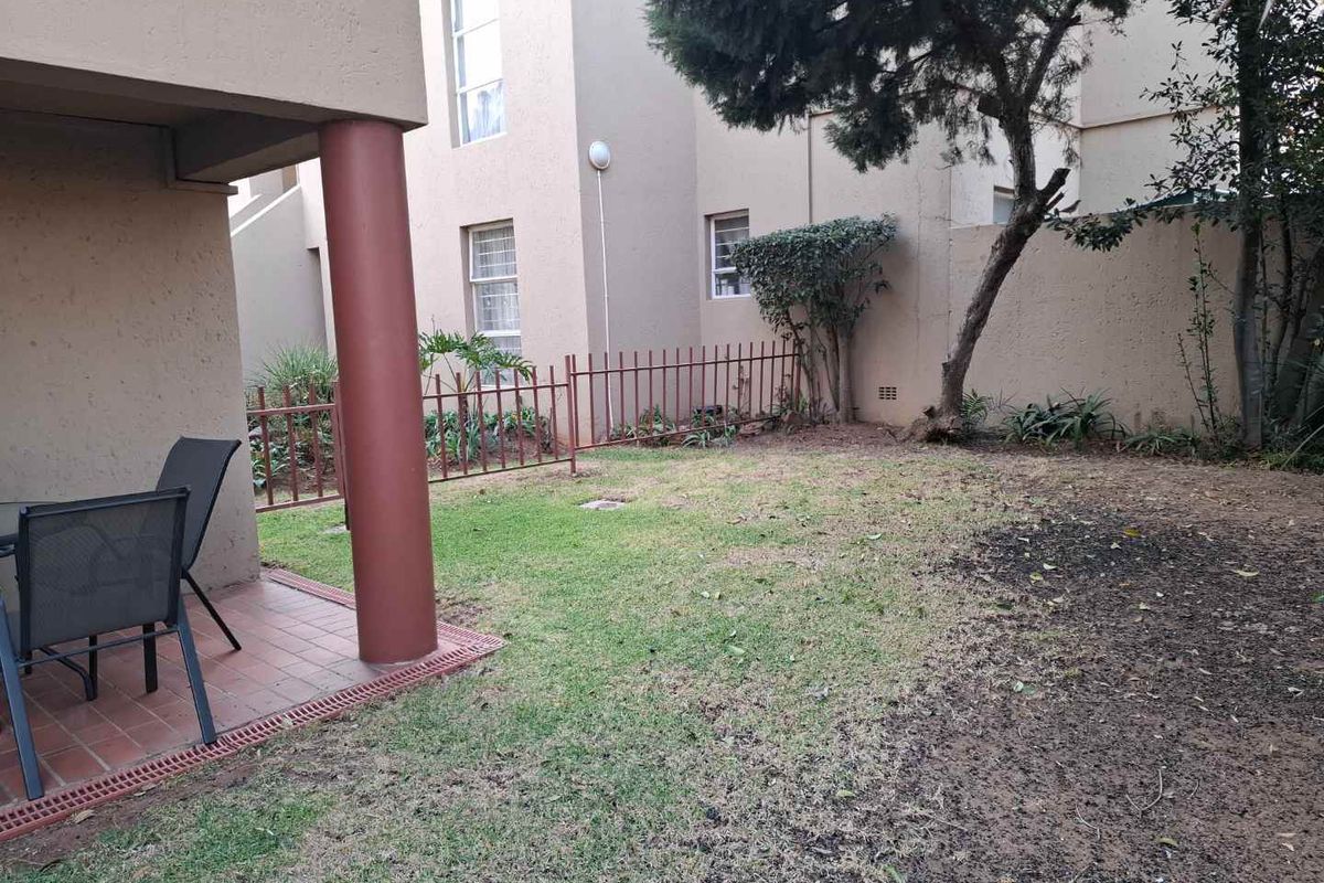 A private rear garden area featuring a paved patio section, lawn, and perimeter fencing, providing an outdoor space for the townhouse.