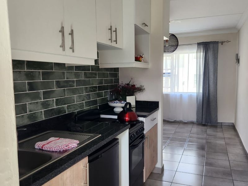 A modern kitchen featuring white upper cabinetry, wood-finish lower cabinets, granite countertops, a dark subway tile backsplash, and tiled flooring.