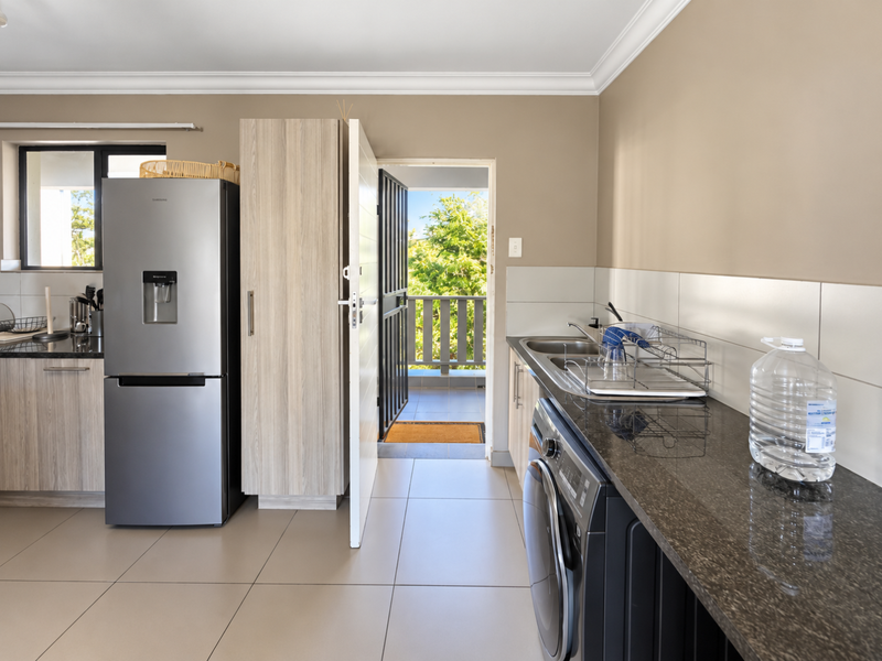 A functional kitchen featuring granite countertops, tiled backsplash, and built-in cabinetry, with direct access to an outdoor balcony area.