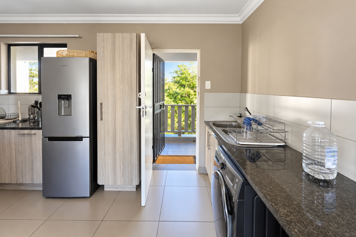 A functional kitchen featuring granite countertops, tiled backsplash, and built-in cabinetry, with direct access to an outdoor balcony area.