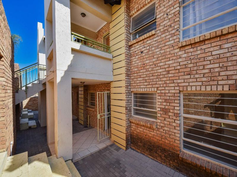 Exterior view of an apartment building featuring face brick walls, a paved courtyard, a balcony, and security features including gates and window bars.