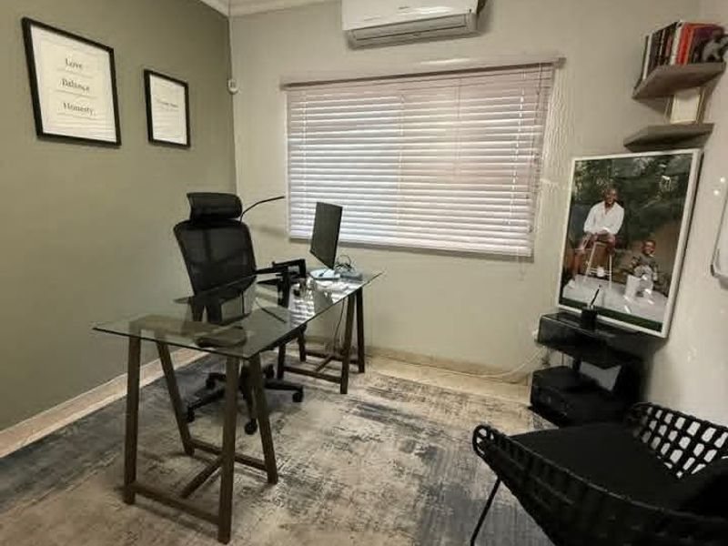 A functional home office featuring tiled flooring, a wall-mounted split-system air conditioner, and venetian blinds for light control.