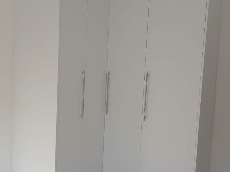 A clean, modern bedroom featuring white built-in cupboards and light-colored tiled flooring with a marble-effect finish.