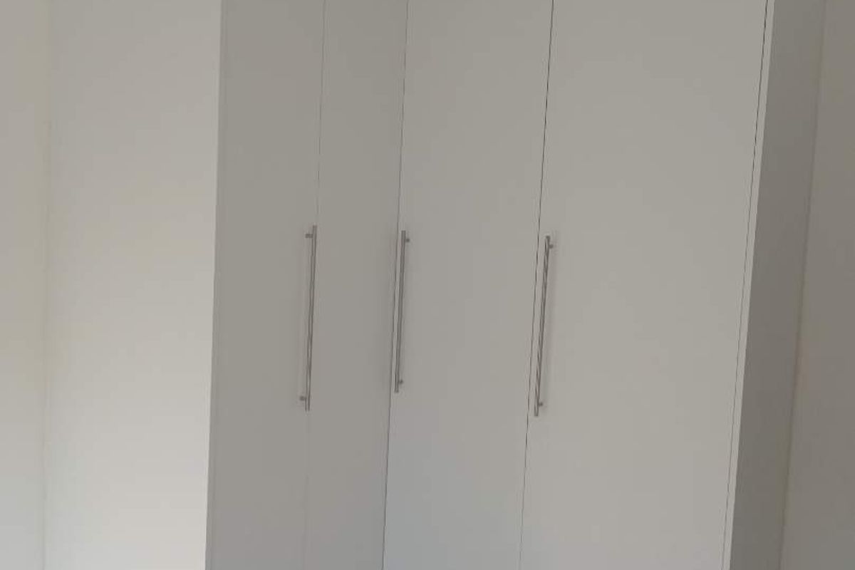A clean, modern bedroom featuring white built-in cupboards and light-colored tiled flooring with a marble-effect finish.