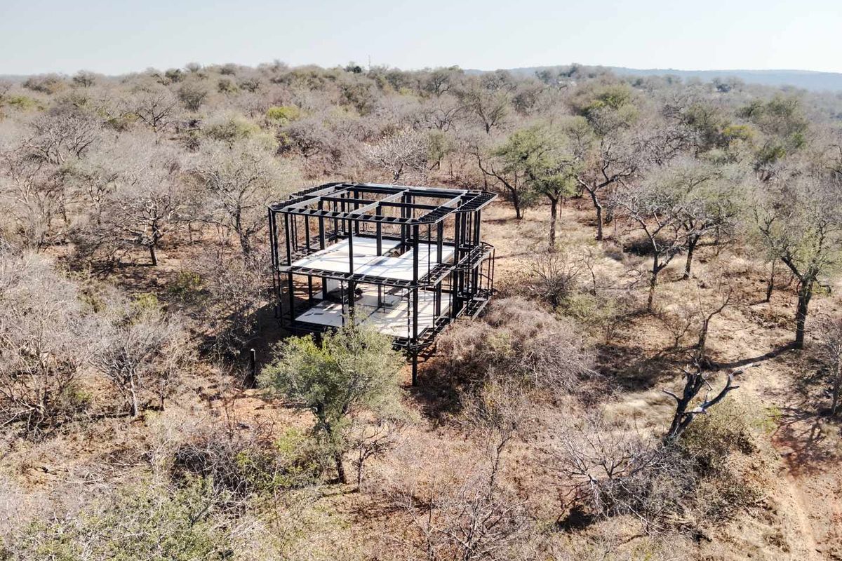 Aerial view of a property under construction, featuring an exposed steel structural frame and concrete floor slabs set within a natural bushveld landscape.