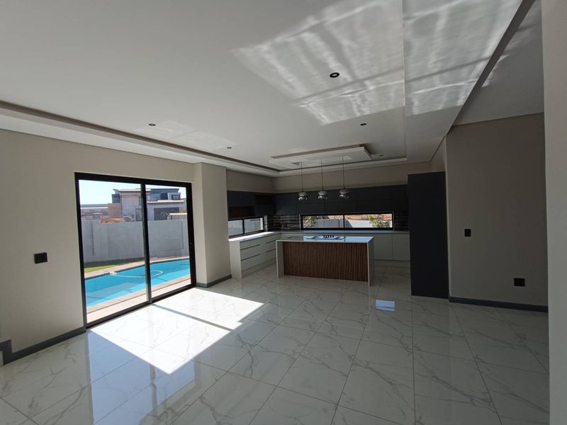 Modern open-plan kitchen and living area featuring sleek cabinetry, a central island, and large sliding doors opening to a swimming pool.
