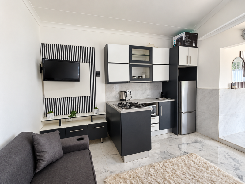 Modern open-plan living area featuring a compact kitchen with built-in cabinetry, gas hob, and elegant marble-look floor and wall tiling.
