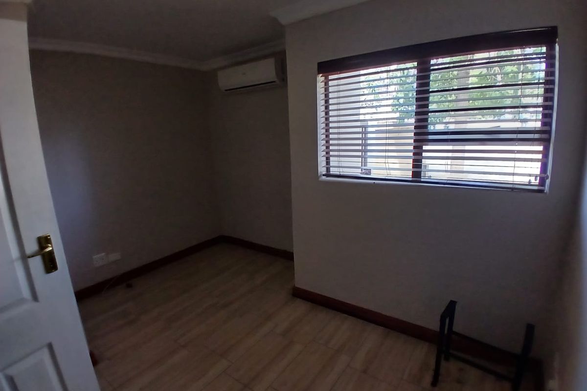 A clean, empty bedroom featuring tiled flooring, an installed air conditioning unit, and window blinds, offering a neutral space ready for occupancy.