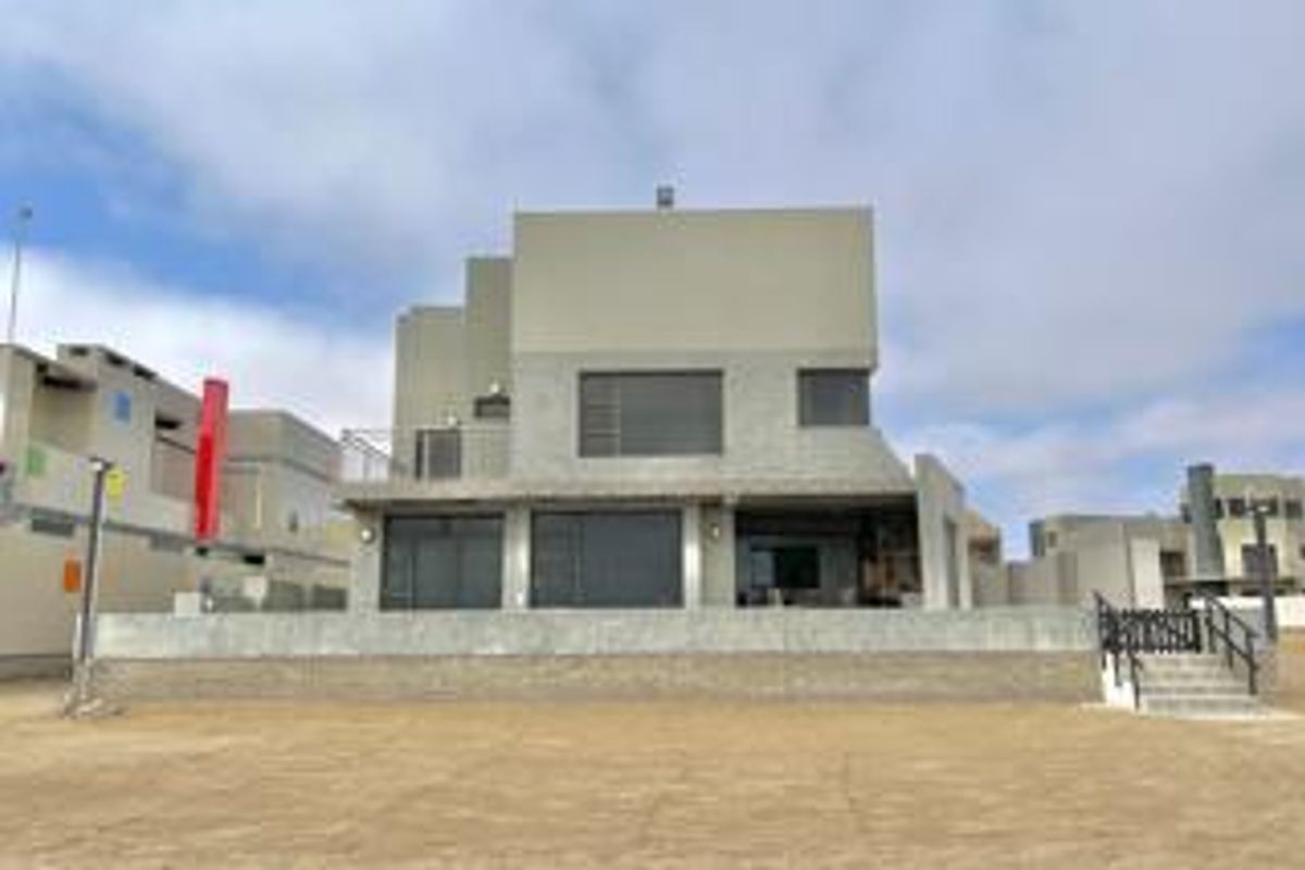 Rear view of a modern multi-level house featuring a raised concrete patio, large glass sliding doors, and a minimalist architectural design.