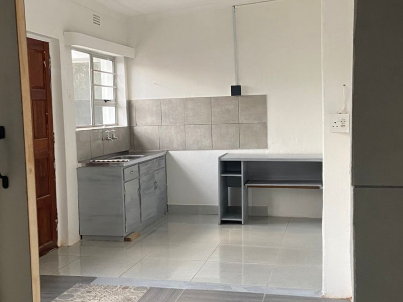 A compact, functional kitchen area featuring tiled flooring, a stainless steel sink, tiled splashback, and basic built-in cabinetry.