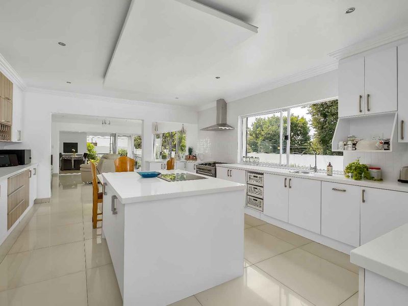 Modern, bright kitchen featuring a central island, sleek white cabinetry, quartz countertops, and high-quality stainless steel appliances, seamlessly flowing into the living area.