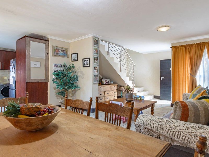 Open-plan living and dining area featuring a functional kitchen with built-in cabinetry, tiled flooring, and a staircase leading to the upper level.