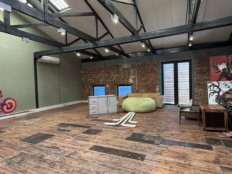 Spacious open-plan office featuring exposed timber roof trusses, brick walls, and timber flooring, offering a unique industrial aesthetic with significant potential for renovation.