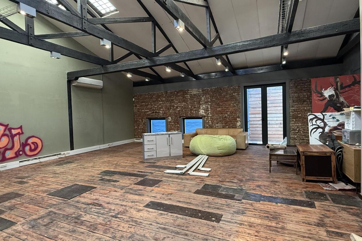 Spacious open-plan office featuring exposed timber roof trusses, brick walls, and timber flooring, offering a unique industrial aesthetic with significant potential for renovation.