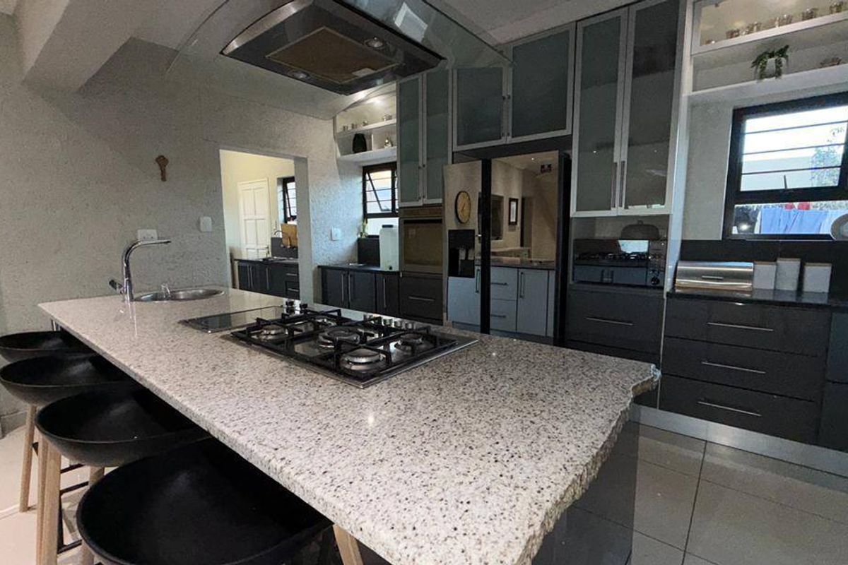 Modern kitchen featuring a large granite-topped island with a built-in gas hob, sleek cabinetry, and integrated stainless steel appliances.