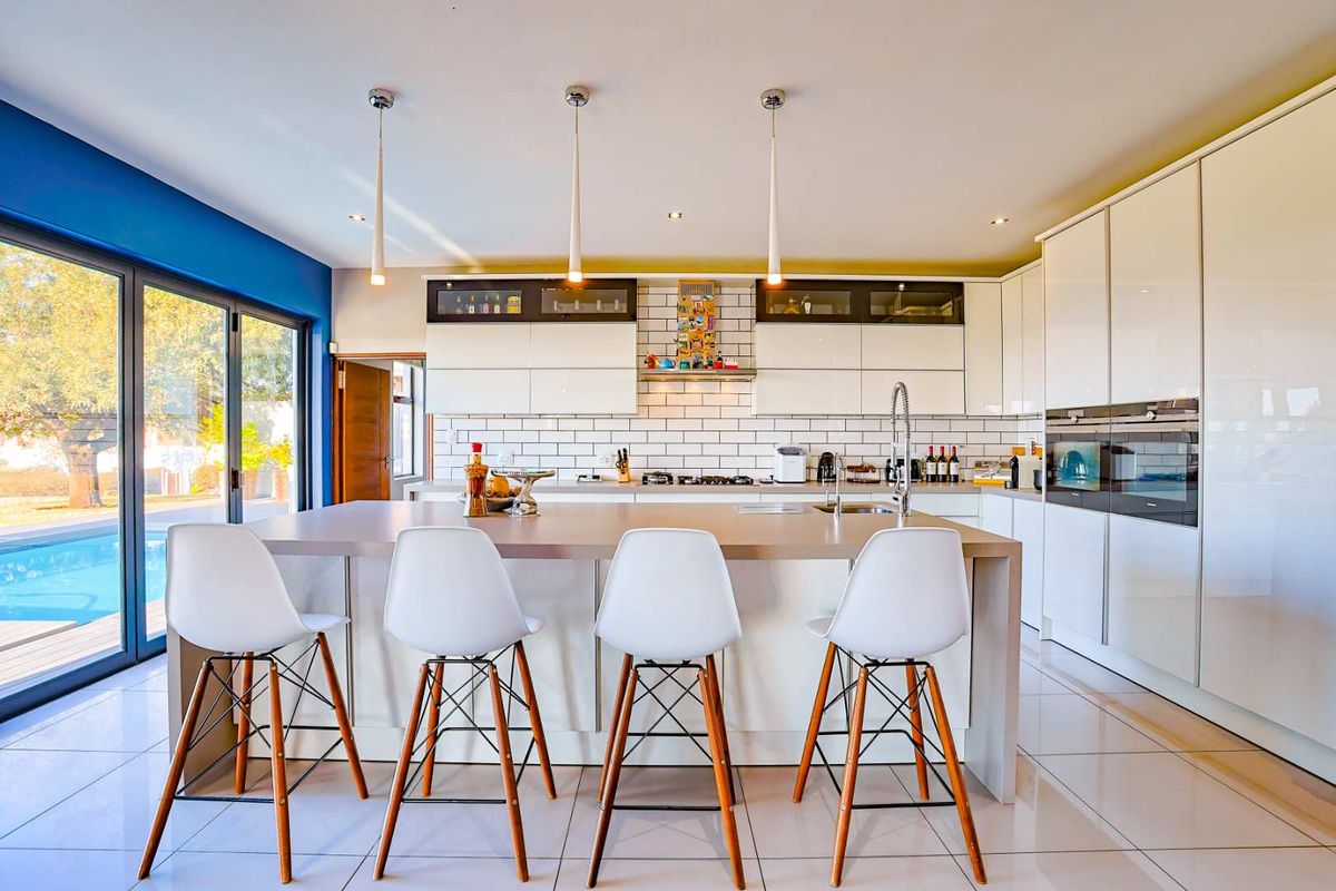 Modern kitchen featuring a large central island, sleek white cabinetry, integrated appliances, subway tile backsplash, and direct access to the outdoor pool area.
