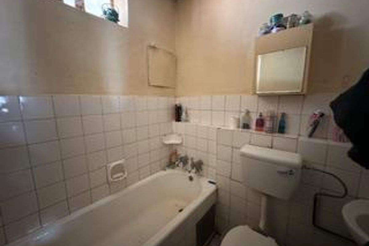 A compact bathroom featuring a standard bathtub, toilet, and wall-mounted medicine cabinet with tiled splashbacks.