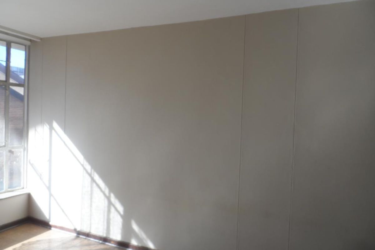 An empty bedroom featuring a large window, neutral wall paneling, and timber-look flooring, offering a blank canvas for personalization.