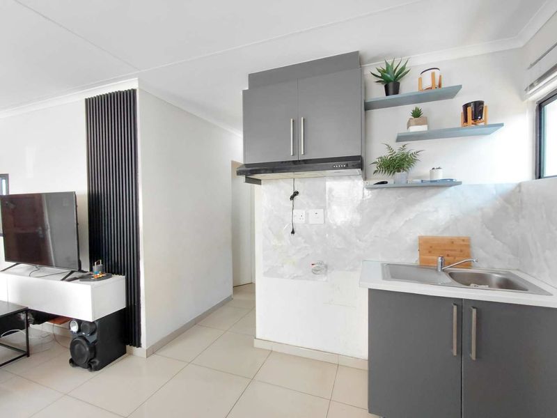 Modern open-plan living area featuring a compact kitchenette with grey cabinetry, stainless steel sink, extractor fan, and a stylish slatted wall accent.