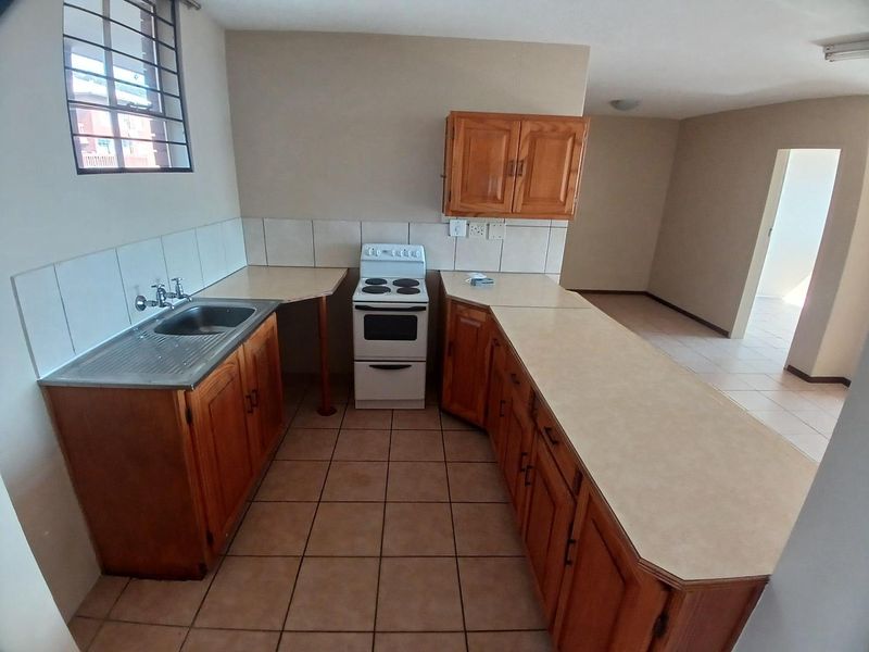 A functional kitchen featuring wooden cabinetry, laminate countertops, a stainless steel sink, and a freestanding stove, with tiled flooring and a tiled backsplash.
