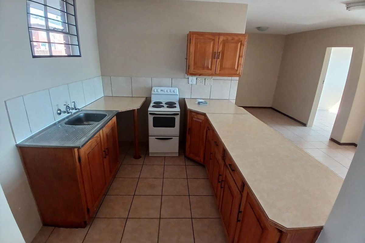 A functional kitchen featuring wooden cabinetry, laminate countertops, a stainless steel sink, and a freestanding stove, with tiled flooring and a tiled backsplash.