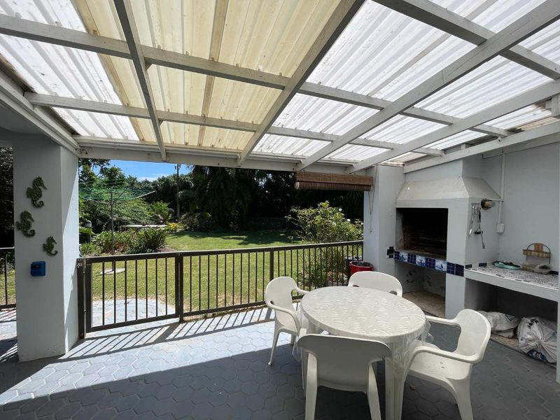 Covered patio area featuring a built-in braai, tiled flooring, and a metal balustrade overlooking the rear garden.