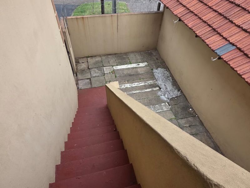 An exterior rear view showing a concrete staircase leading down to a paved courtyard area enclosed by perimeter walls.