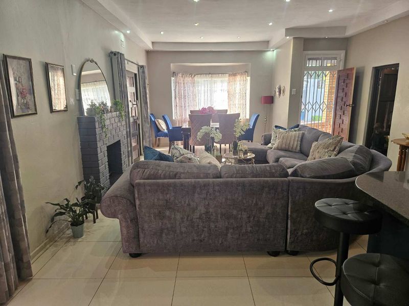 Spacious open-plan living and dining area featuring tiled flooring, a brick fireplace, and recessed downlighting, creating a comfortable and functional family space.