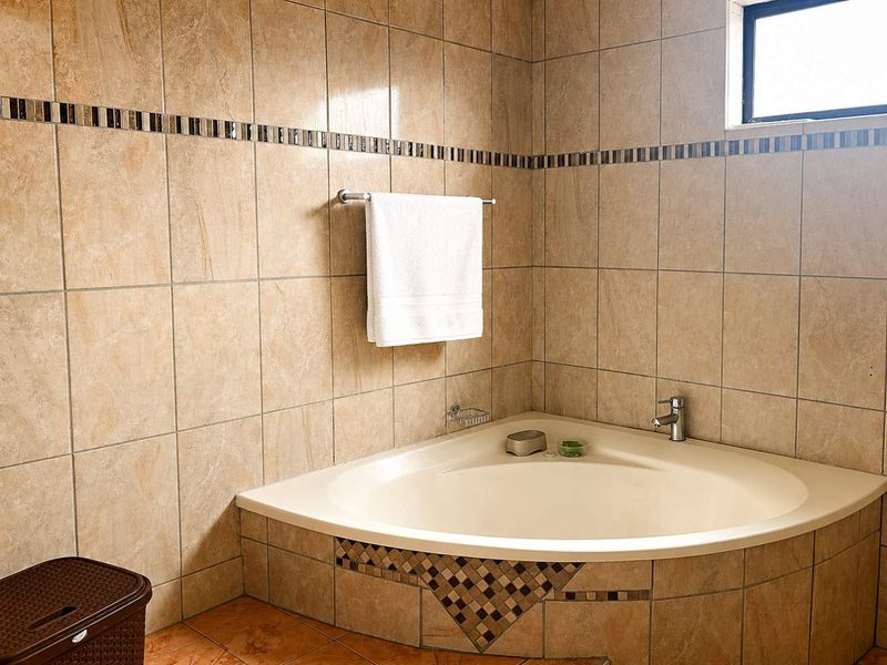 A bathroom featuring a corner bathtub with a tiled surround, chrome mixer tap, and decorative mosaic tile accents on the walls.