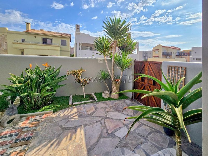 A private rear courtyard featuring natural stone paving, a solid boundary wall, and a wooden access gate.