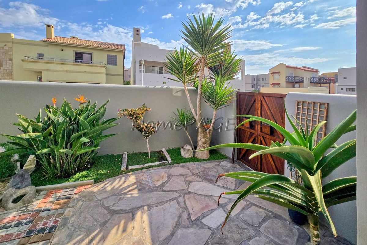A private rear courtyard featuring natural stone paving, a solid boundary wall, and a wooden access gate.
