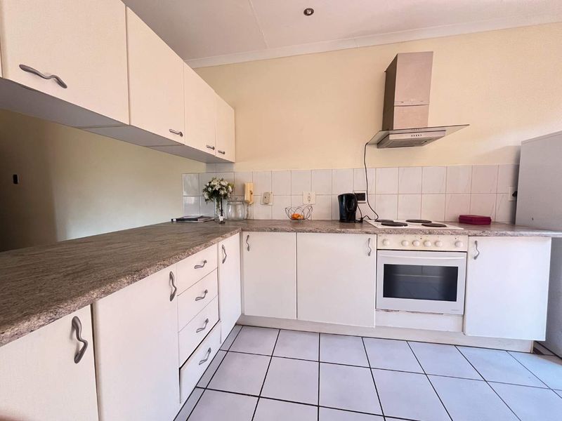 A functional kitchen featuring white cabinetry, laminate countertops, a built-in oven with extractor fan, and tiled flooring.