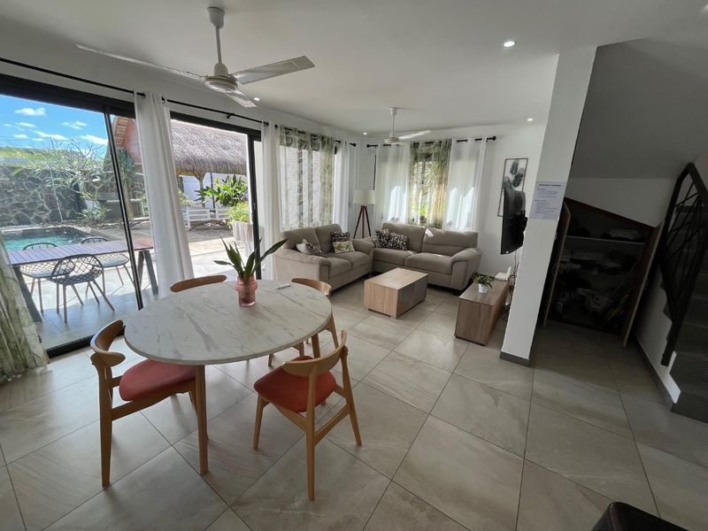 Bright open-plan living and dining area featuring large sliding glass doors that open onto a patio and pool area, with neutral tiled flooring throughout.