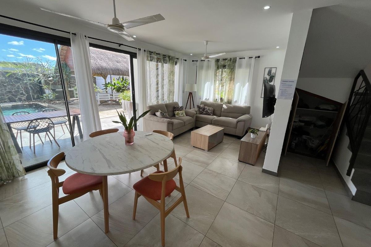 Bright open-plan living and dining area featuring large sliding glass doors that open onto a patio and pool area, with neutral tiled flooring throughout.