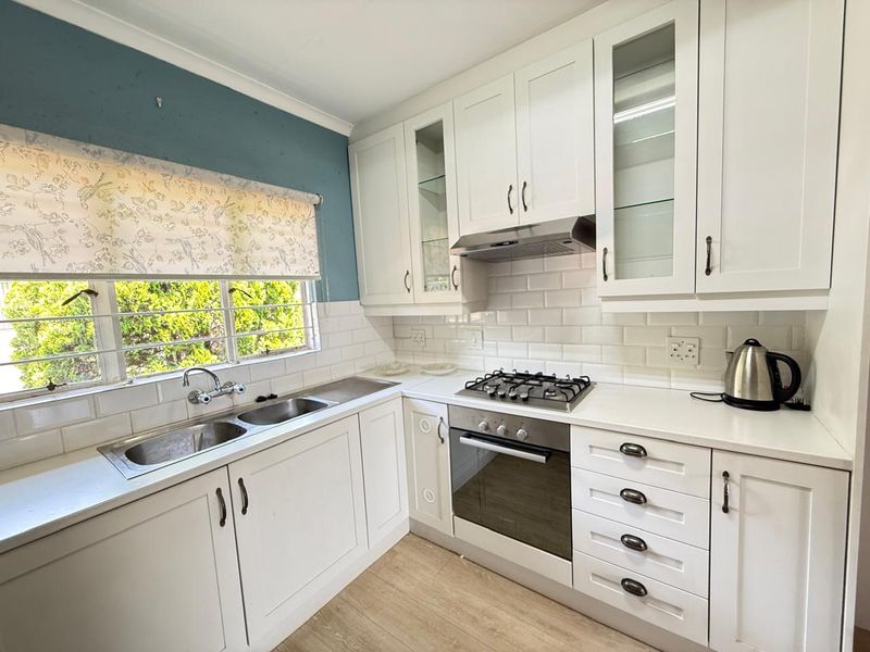 A well-maintained kitchen featuring white shaker-style cabinetry, subway tile backsplash, integrated gas hob, built-in oven, and a stainless steel double sink.