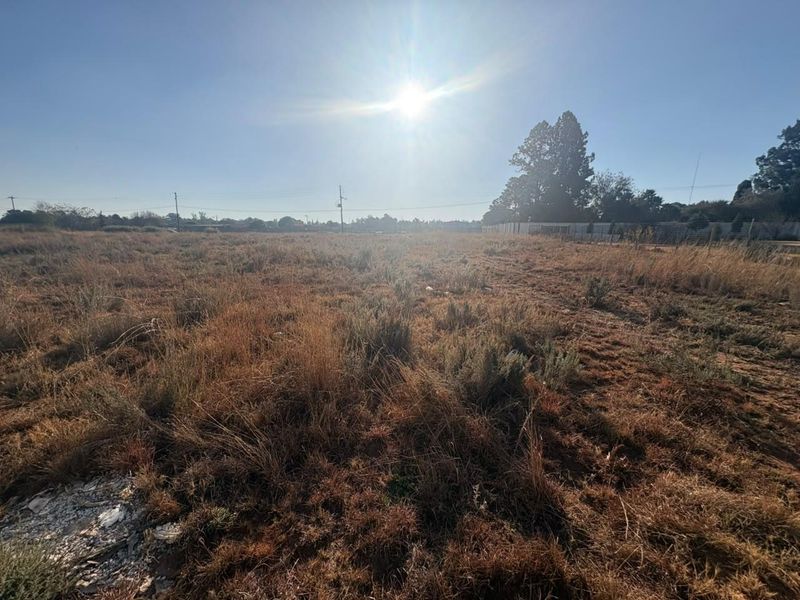A wide-angle view of a vacant residential plot featuring dry grass and overhead utility lines under a clear sky.