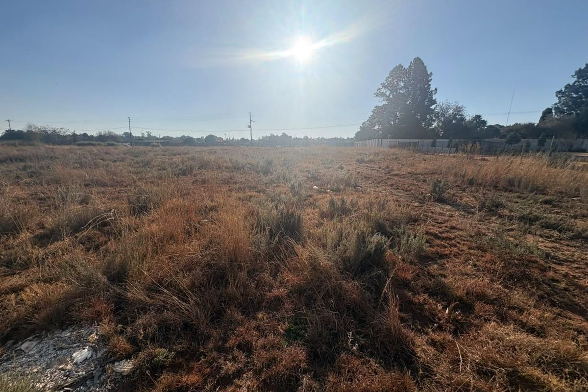 A wide-angle view of a vacant residential plot featuring dry grass and overhead utility lines under a clear sky.