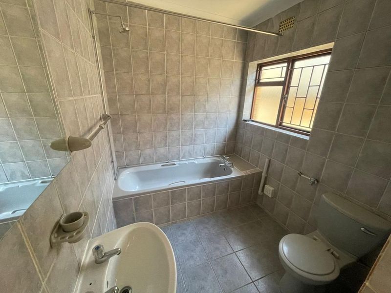 A functional bathroom featuring a built-in bathtub with shower, pedestal basin, and toilet, finished with neutral ceramic wall and floor tiles.