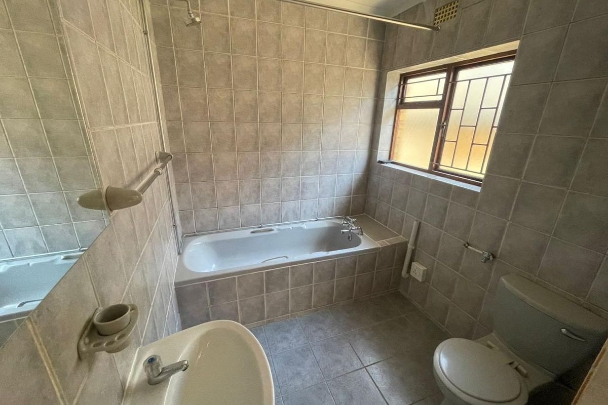 A functional bathroom featuring a built-in bathtub with shower, pedestal basin, and toilet, finished with neutral ceramic wall and floor tiles.
